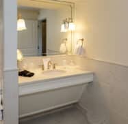 A clean bathroom with a marble sink countertop, a mirror bordered by lights, and folded towels on the left.