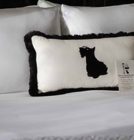 A rectangular pillow with a black dog silhouette is placed on a white bed, accompanied by a small informational card.