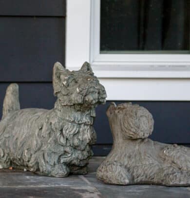 Two stone dog sculptures are placed on a patio in front of a window.