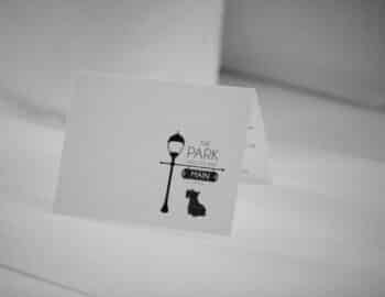 A black and white card artfully captures a streetlamp with a "The Park On Main" sign, featuring the silhouette of a small dog nearby—a charming scene reminiscent of downtown near the Highlands NC hotel.