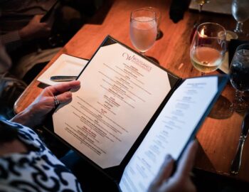 Person holding a menu at a restaurant table, with water and wine glasses in the background.